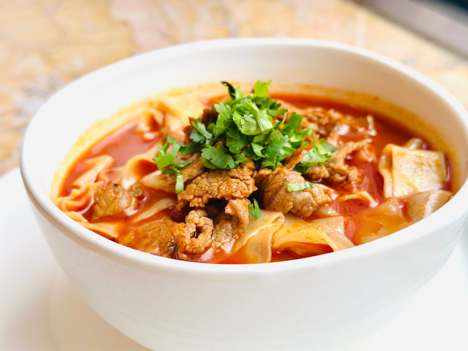 A bowl of clear beef noodle soup with coriander