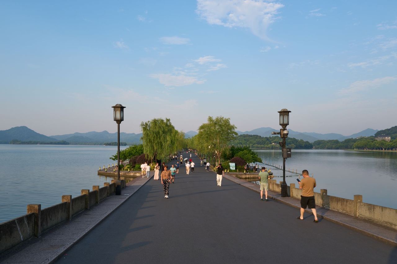 A tree-lined causeway crossing West Lake, with the hills beyond